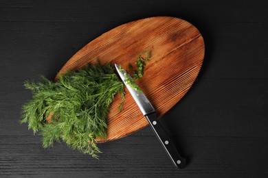 Photo of Sprigs of fresh green dill and knife on black wooden table, top view