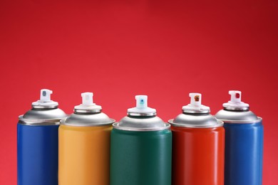 Many spray paint cans on red background. Space for text