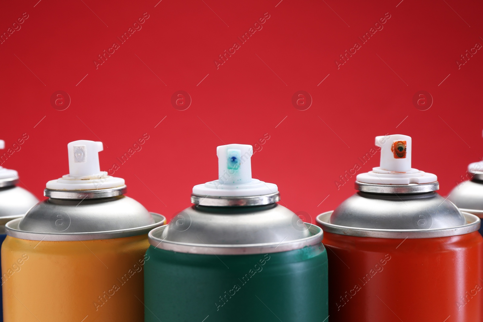 Photo of Many spray paint cans on red background, closeup