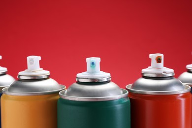 Photo of Many spray paint cans on red background, closeup