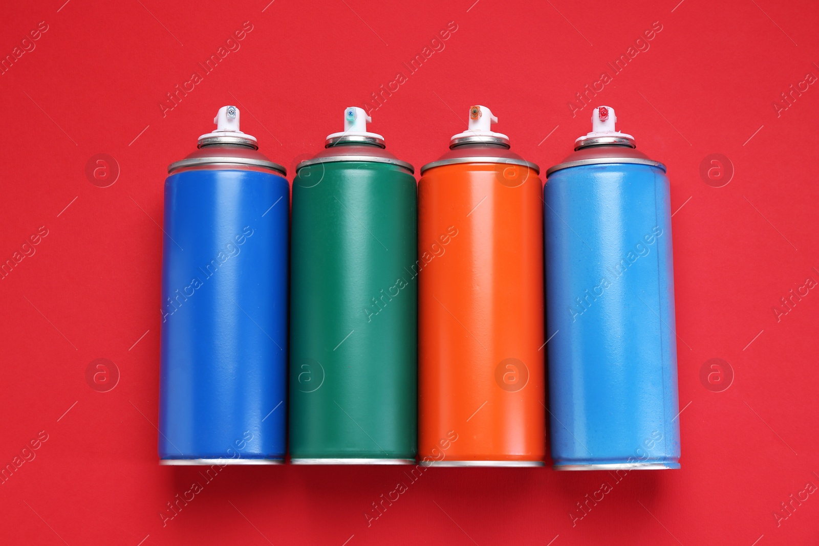 Photo of Many spray paint cans on red background, top view