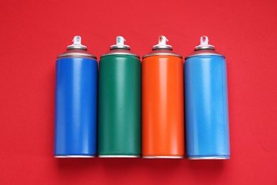 Many spray paint cans on red background, top view