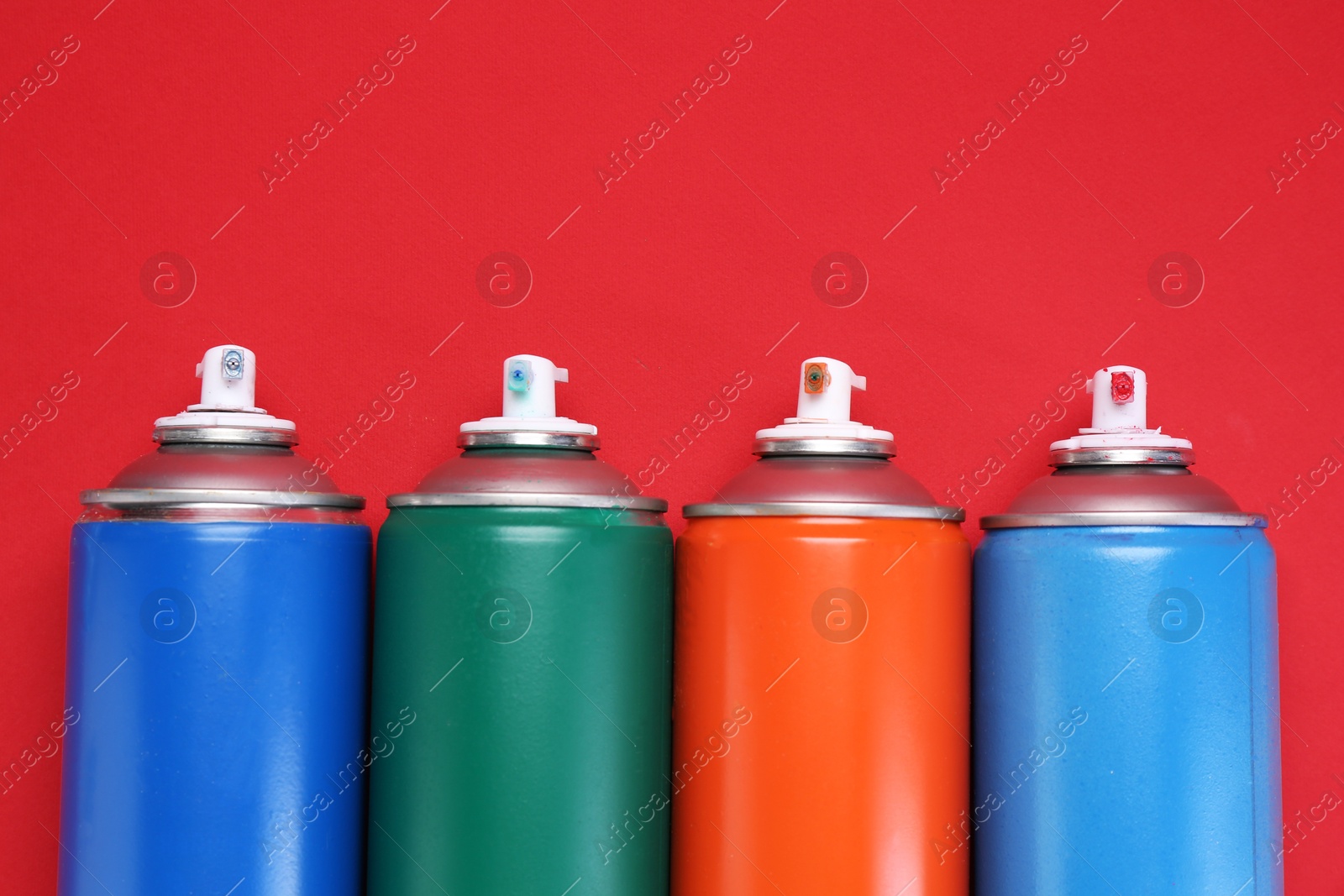 Photo of Many spray paint cans on red background, top view