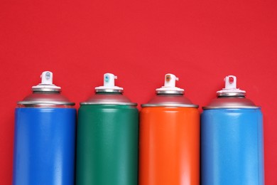 Photo of Many spray paint cans on red background, top view