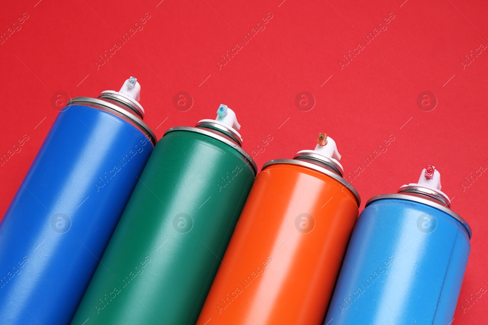 Photo of Many spray paint cans on red background, closeup