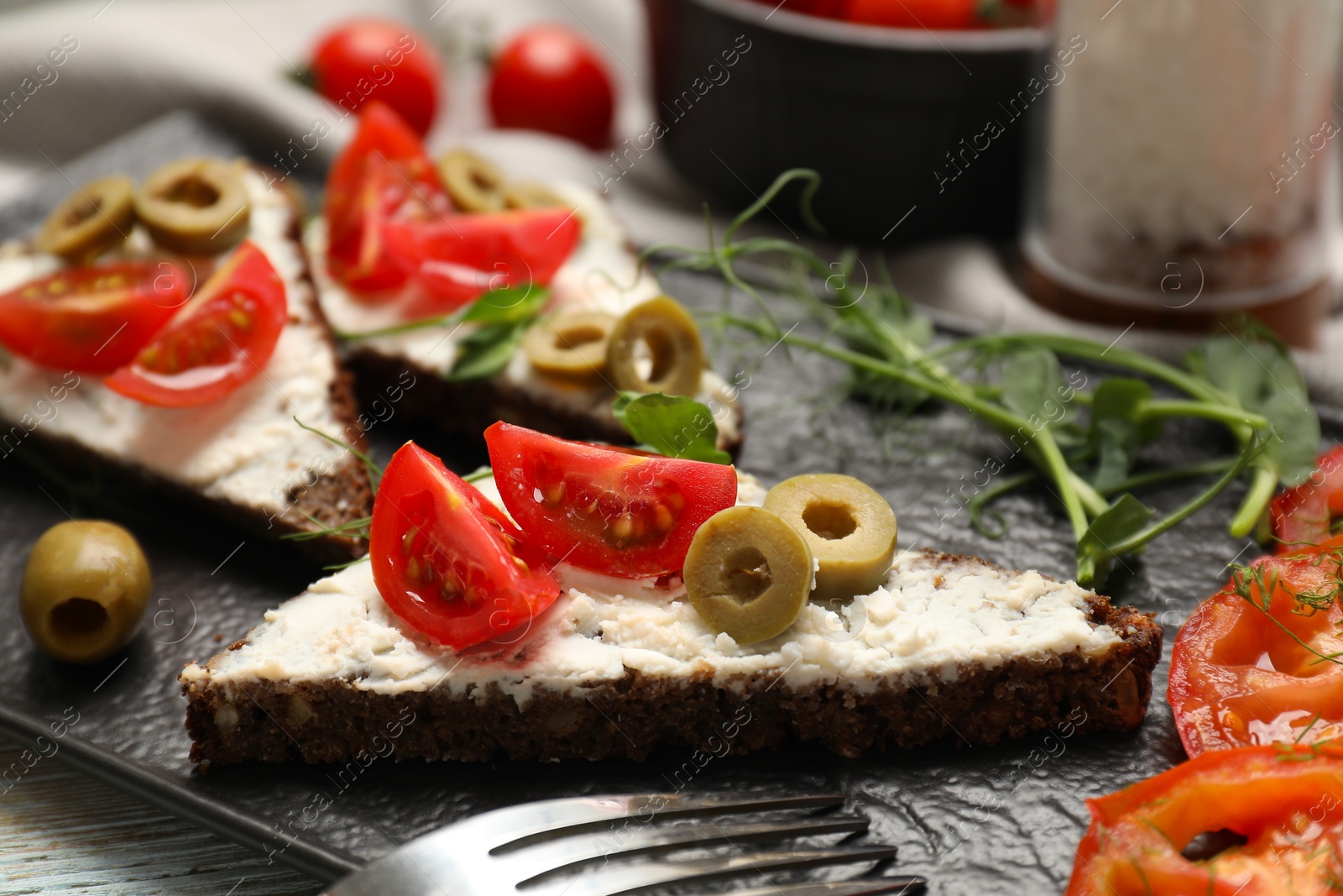 Photo of Delicious ricotta bruschettas with fresh tomatoes, olives and greens on table, closeup