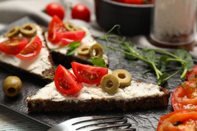 Delicious ricotta bruschettas with fresh tomatoes, olives and greens on table, closeup