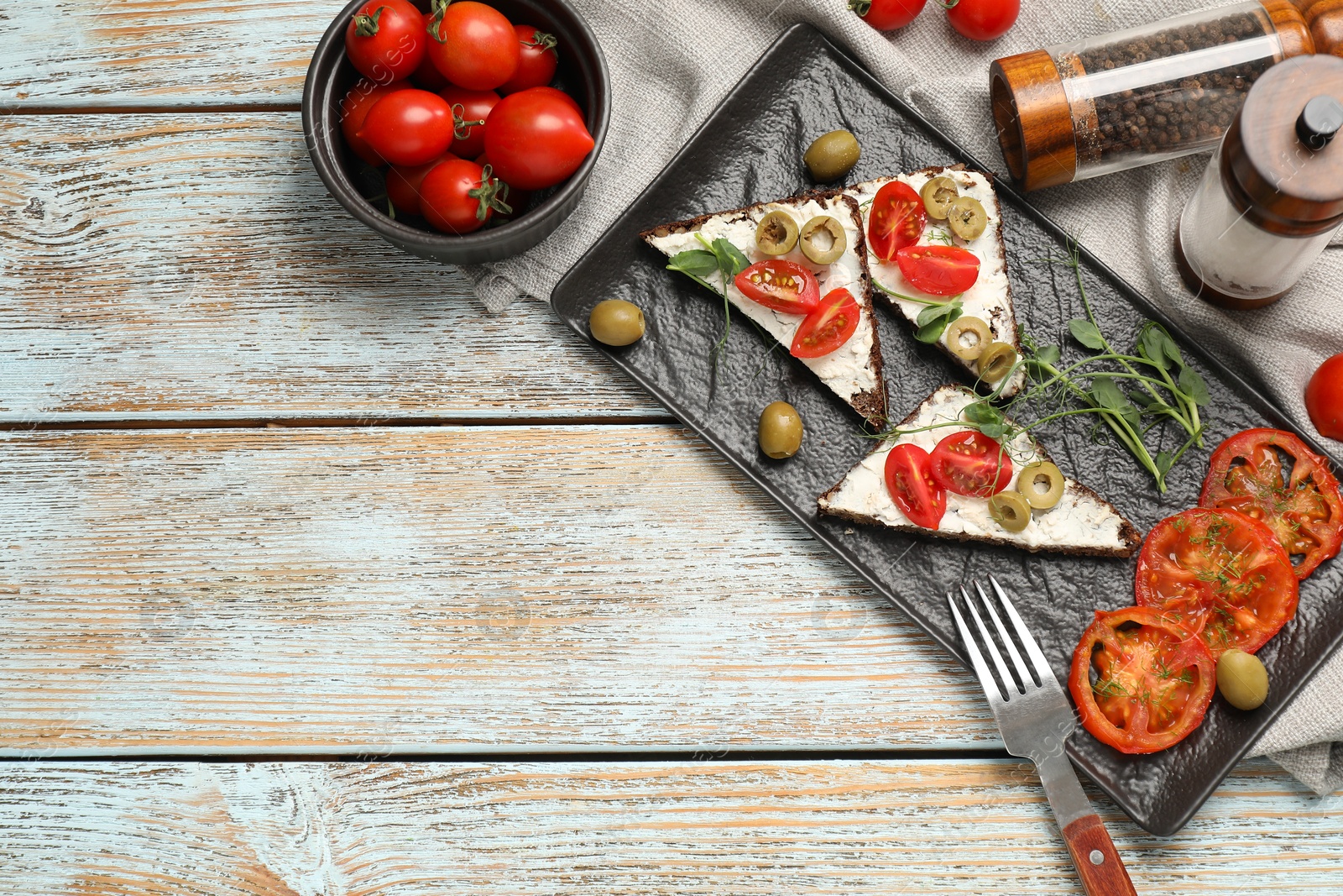 Photo of Delicious ricotta bruschettas with fresh tomatoes, olives and greens on wooden table, flat lay. Space for text