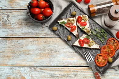 Delicious ricotta bruschettas with fresh tomatoes, olives and greens on wooden table, flat lay. Space for text