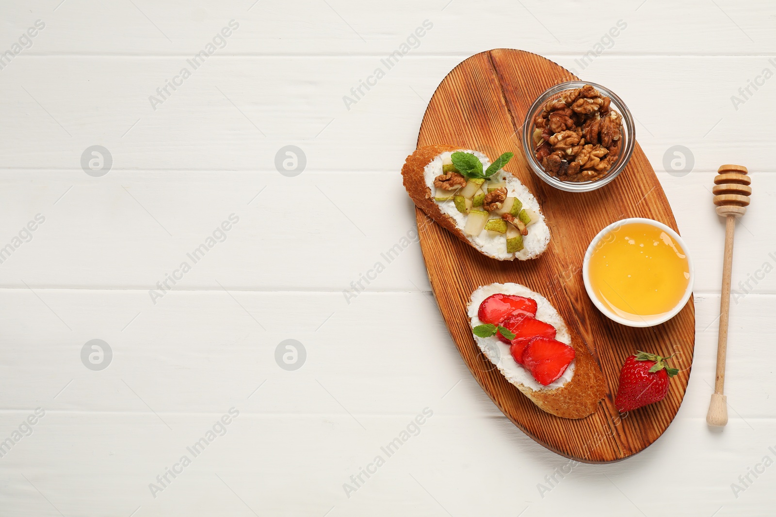 Photo of Delicious ricotta bruschettas with pear, strawberry and walnut on white wooden table, top view. Space for text