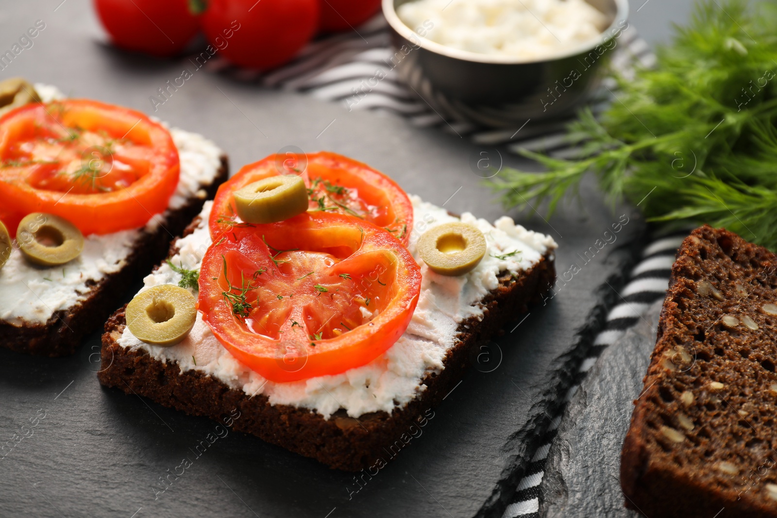 Photo of Delicious ricotta bruschettas with sliced tomatoes, olives and greens on black table, closeup