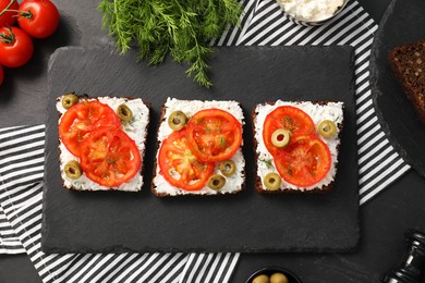 Delicious ricotta bruschettas with sliced tomatoes, olives and greens on black table, flat lay