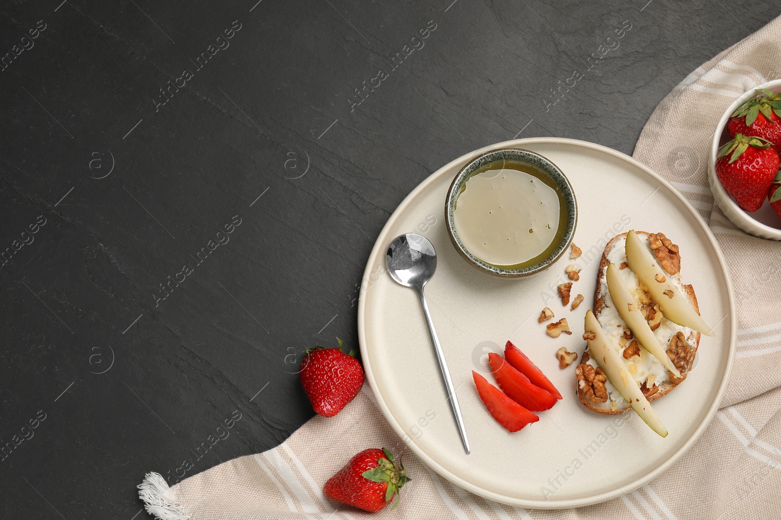 Photo of Delicious ricotta bruschetta with pear, strawberry and walnut on black table, flat lay. Space for text