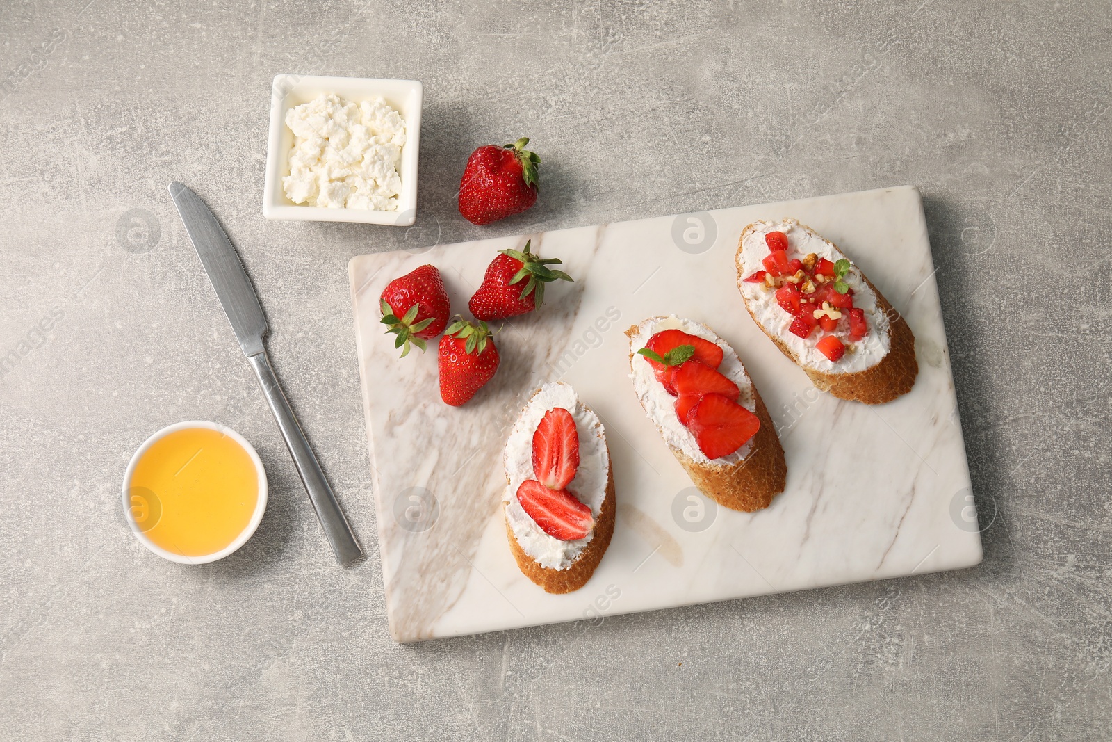 Photo of Delicious ricotta bruschettas with strawberry and mint on grey table, flat lay