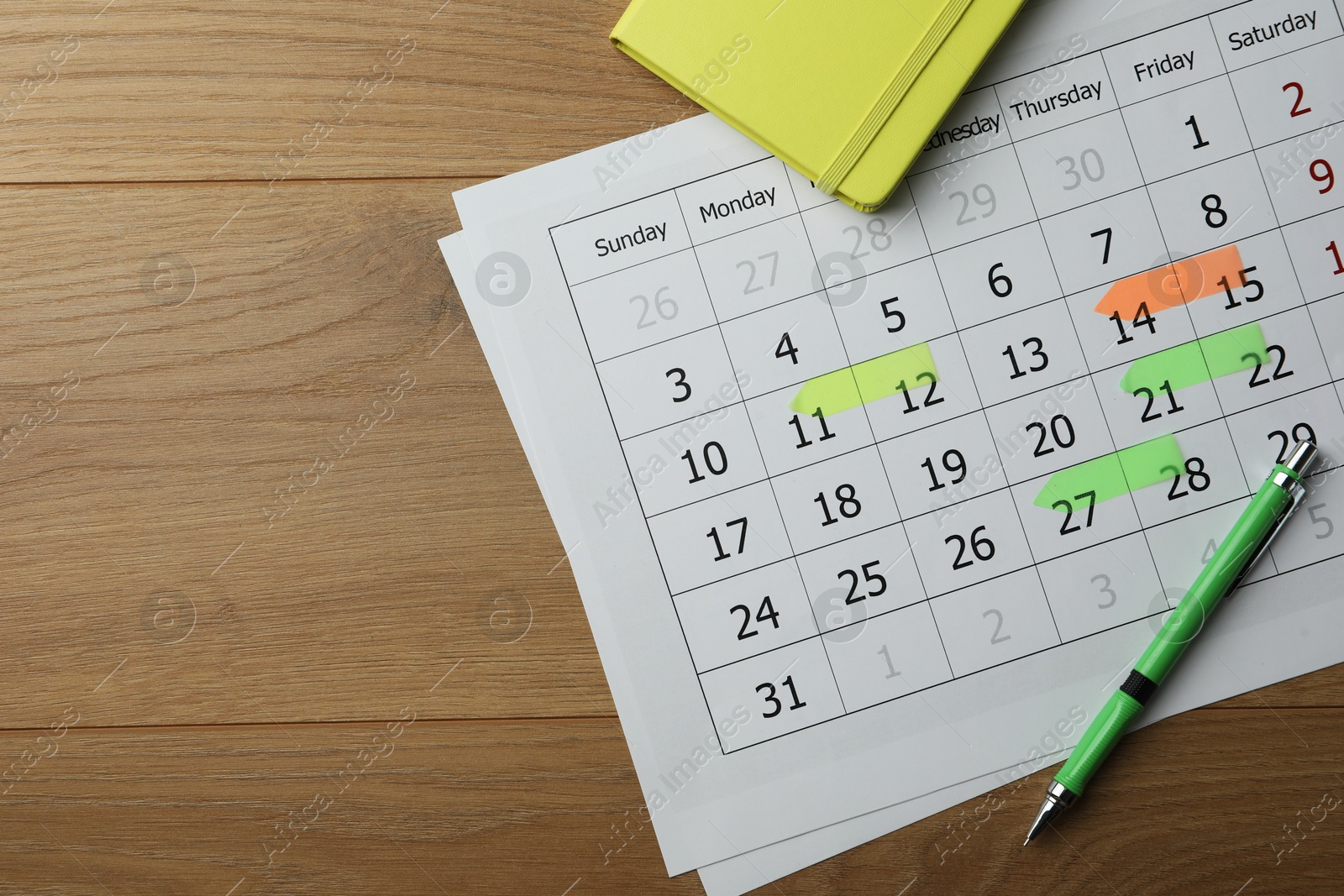 Photo of Timetable. Calendar page with marked dates, pen and notebook on wooden table, top view. Space for text