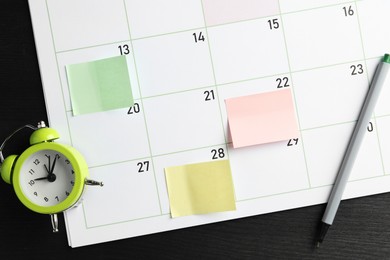 Photo of Timetable. Planner with sticky notes, pen and alarm clock on black wooden table, top view