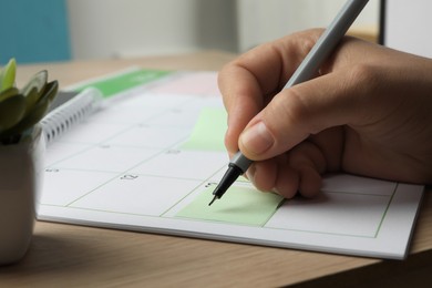 Photo of Timetable. Man making schedule using calendar and sticky note at wooden table, closeup