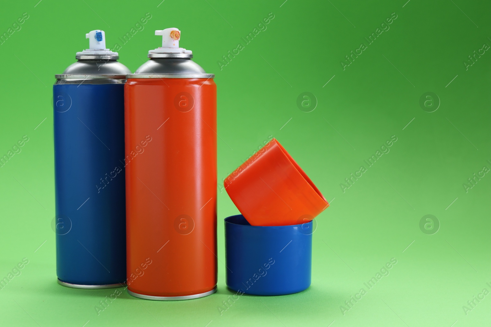 Photo of Two spray paint cans on green background, space for text