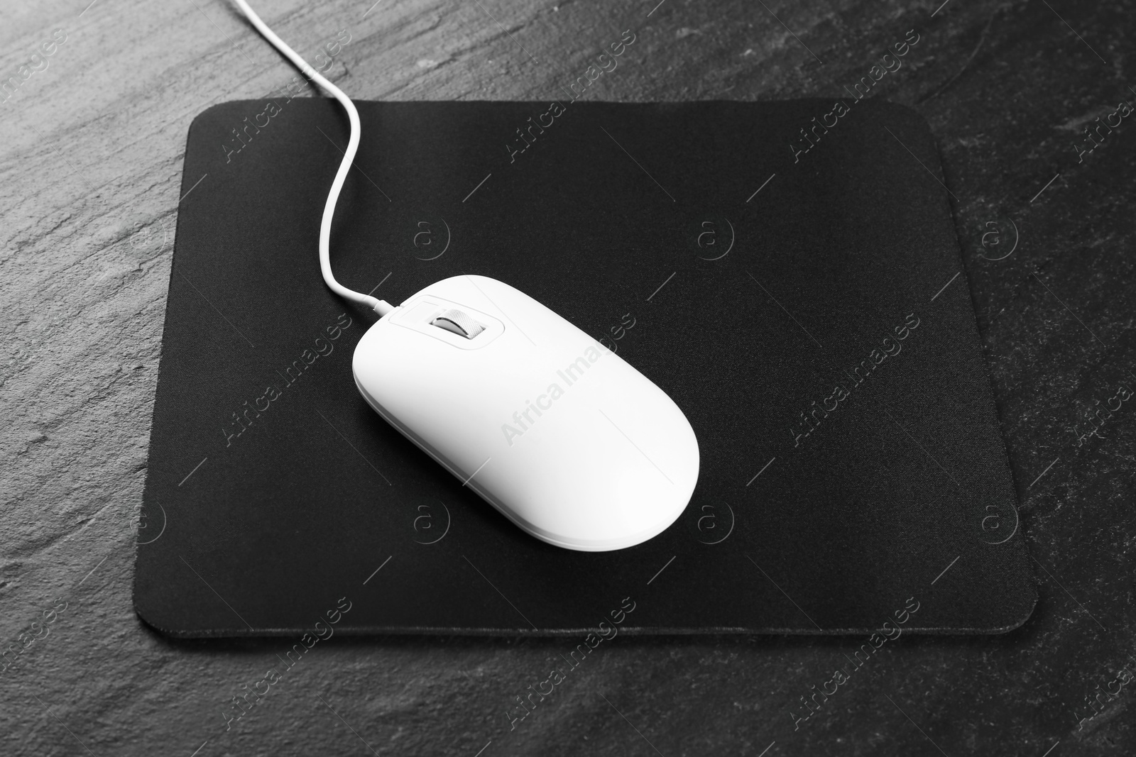 Photo of White wired mouse and mousepad on black textured table