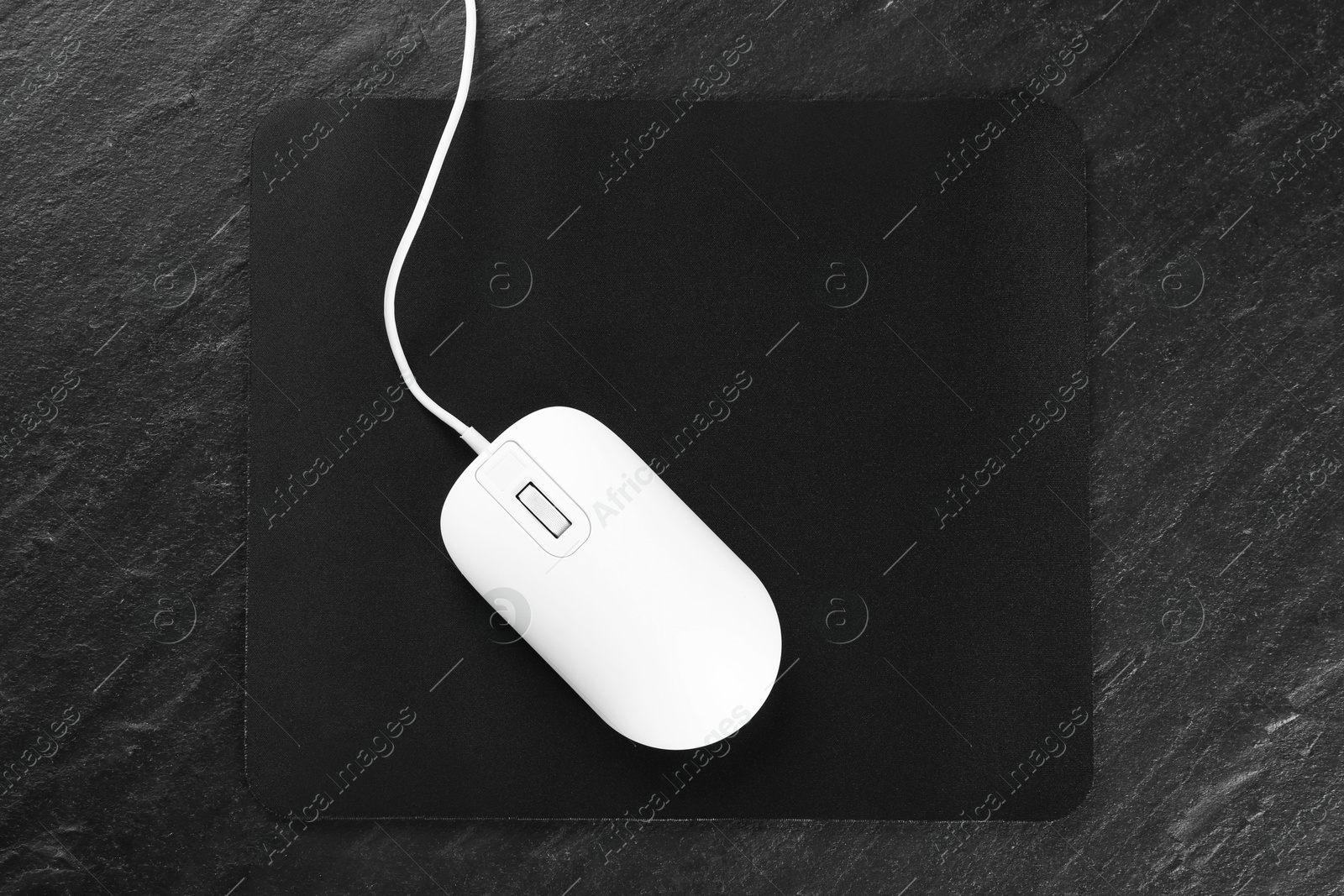 Photo of White wired mouse and mousepad on black textured table, top view