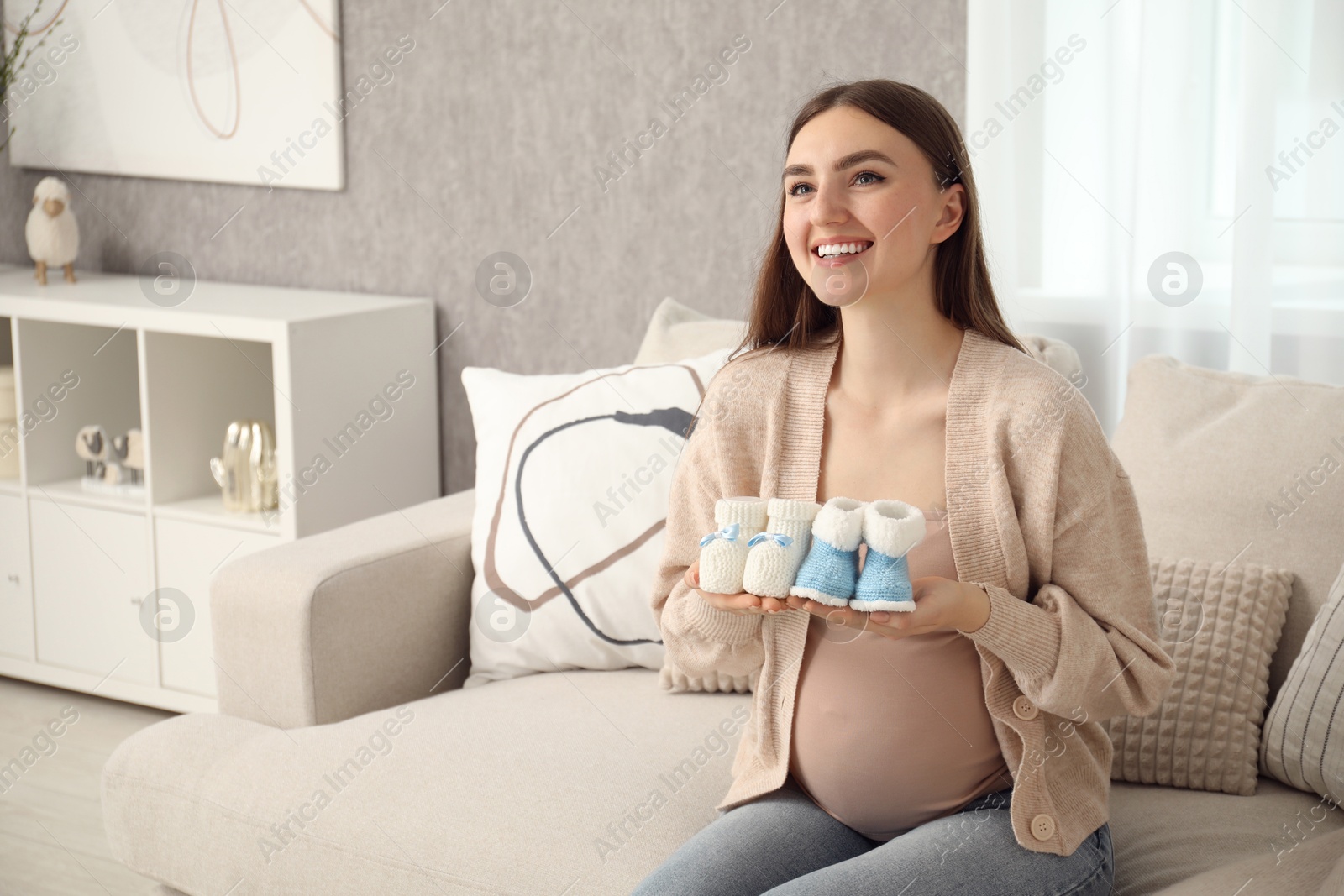 Photo of Expecting twins. Pregnant woman holding two pairs of shoes at home, space for text