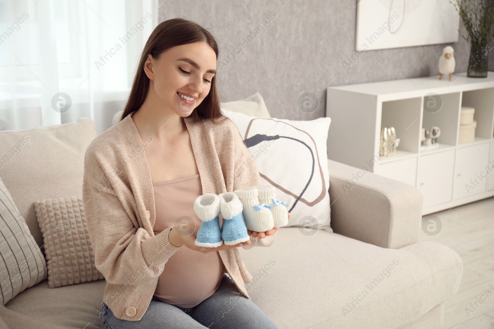 Photo of Expecting twins. Pregnant woman holding two pairs of shoes at home, space for text