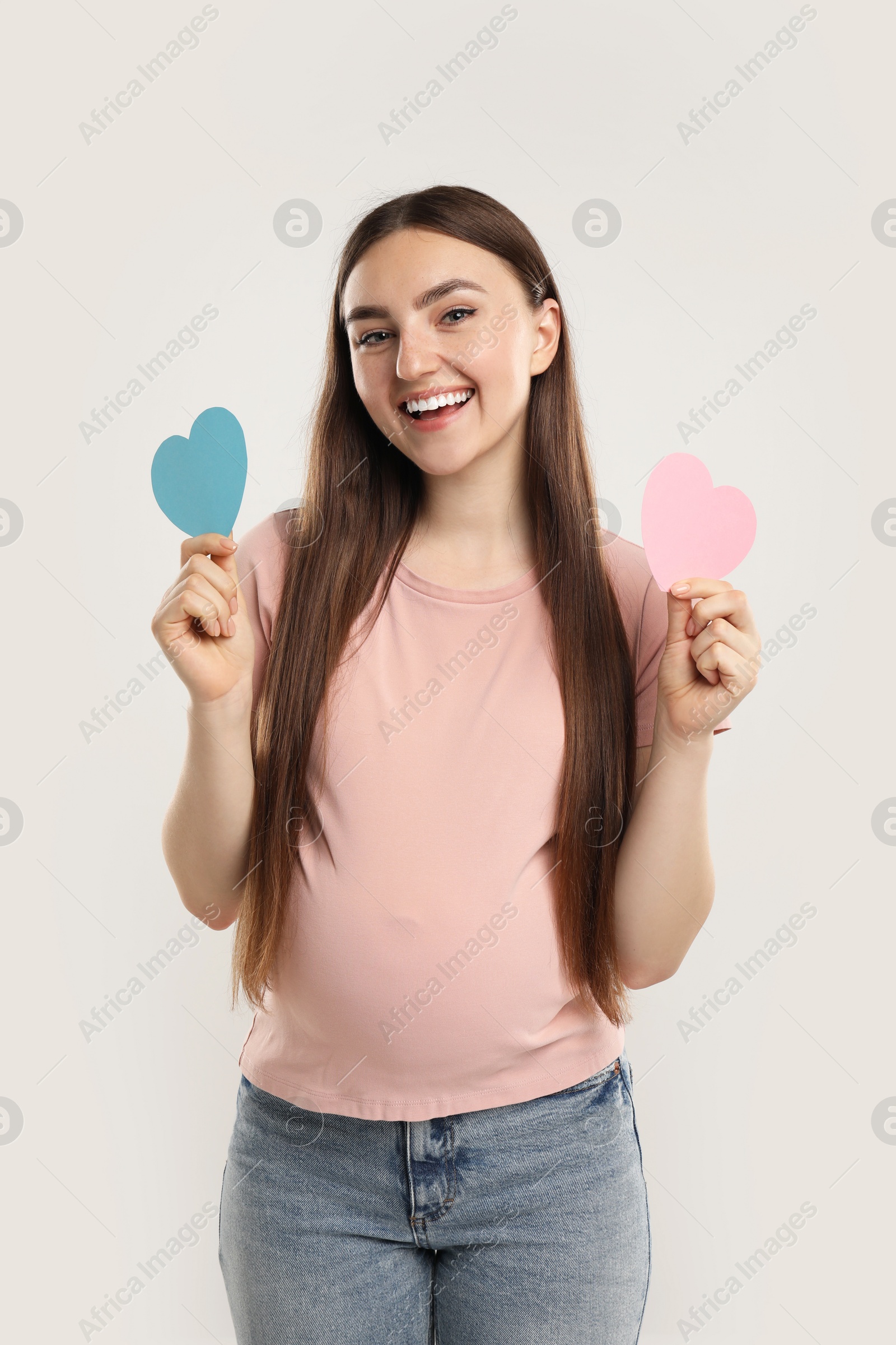 Photo of Expecting twins. Pregnant woman holding two paper cutouts of hearts on light grey background