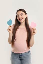 Photo of Expecting twins. Pregnant woman holding two paper cutouts of hearts on light grey background
