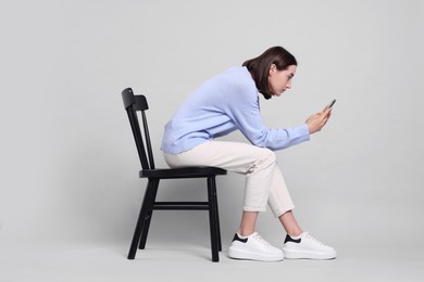 Photo of Woman with poor posture sitting on chair and using smartphone against gray background