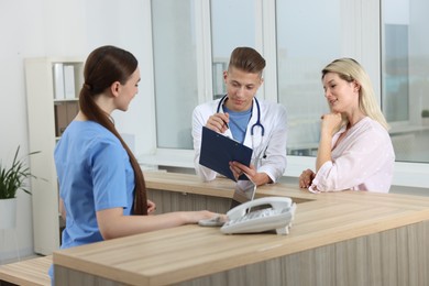 Photo of Professional receptionist and doctor working with patient at wooden desk in hospital