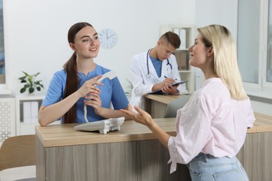 Photo of Professional receptionist and doctor working with patient at wooden desk in hospital