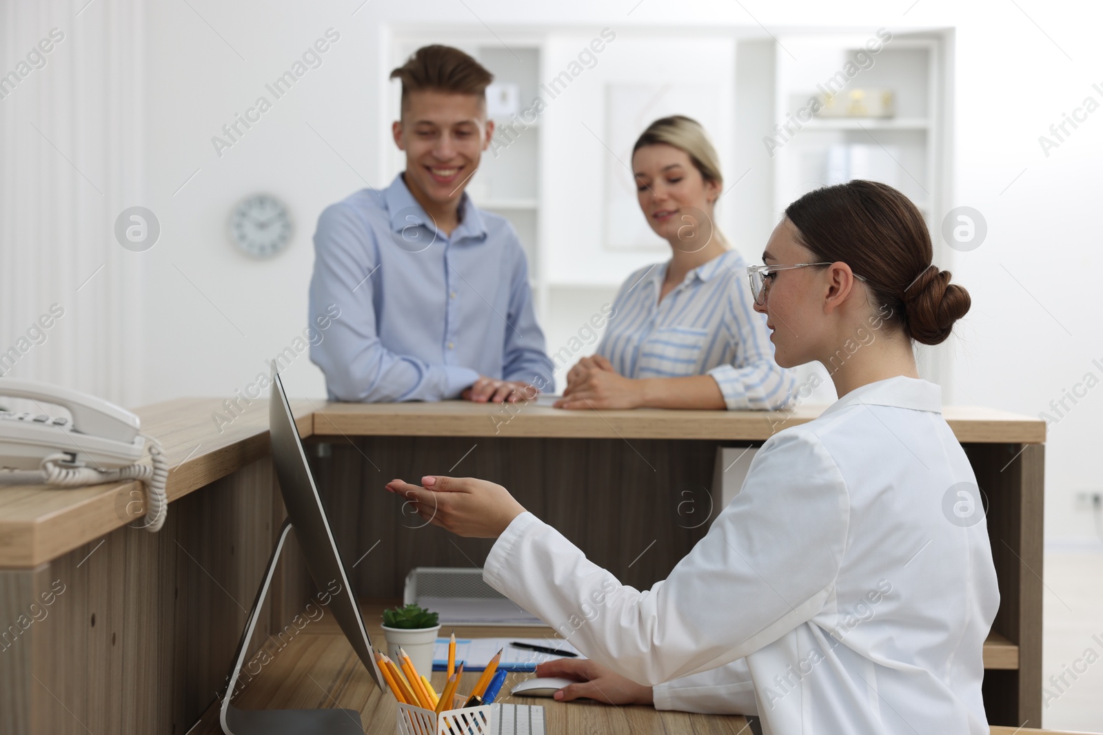 Photo of Professional receptionist working with patients at wooden desk in hospital