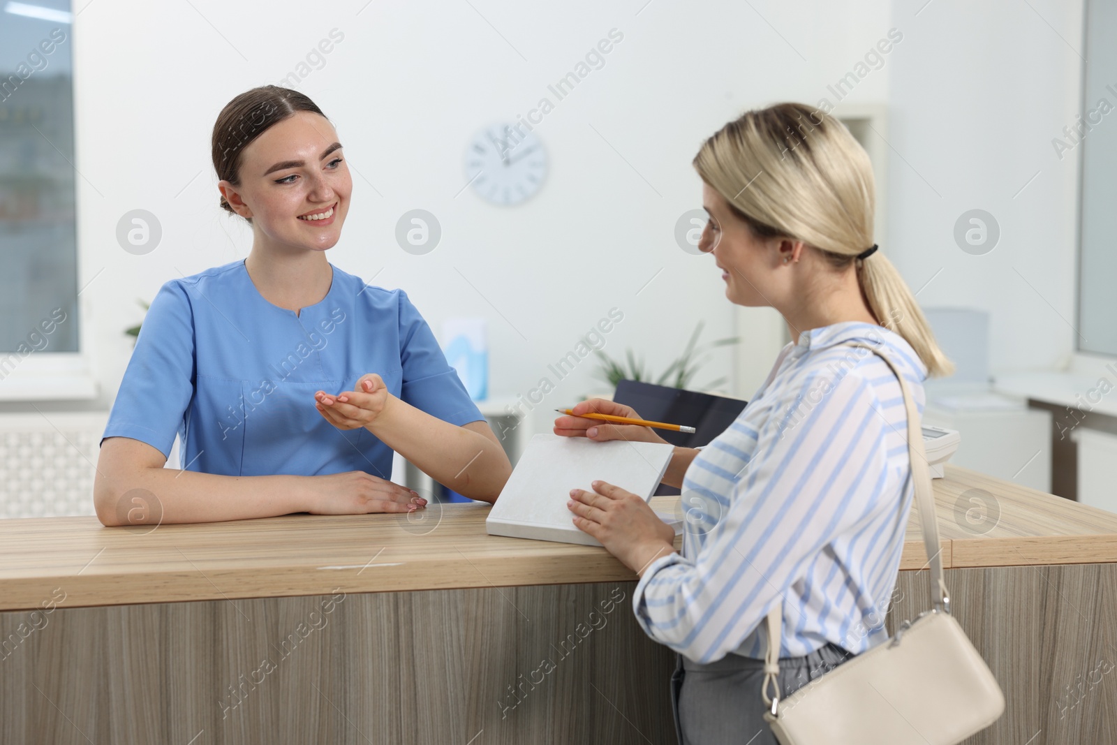 Photo of Professional receptionist working with patient at wooden desk in hospital