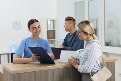 Photo of Professional receptionist working with patients at wooden desk in hospital