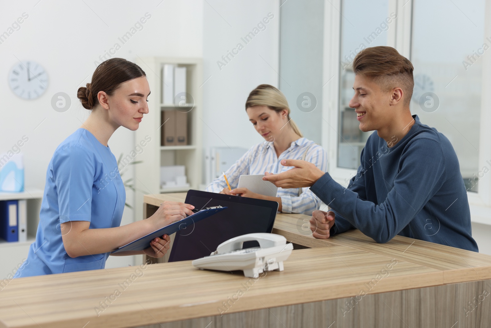 Photo of Professional receptionist working with patients at wooden desk in hospital