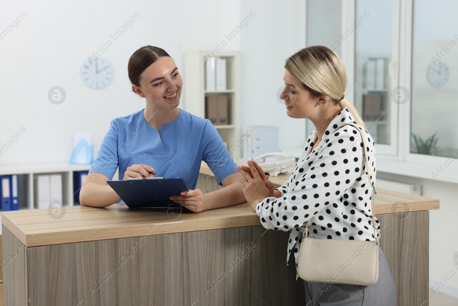 Photo of Professional receptionist working with patient at wooden desk in hospital