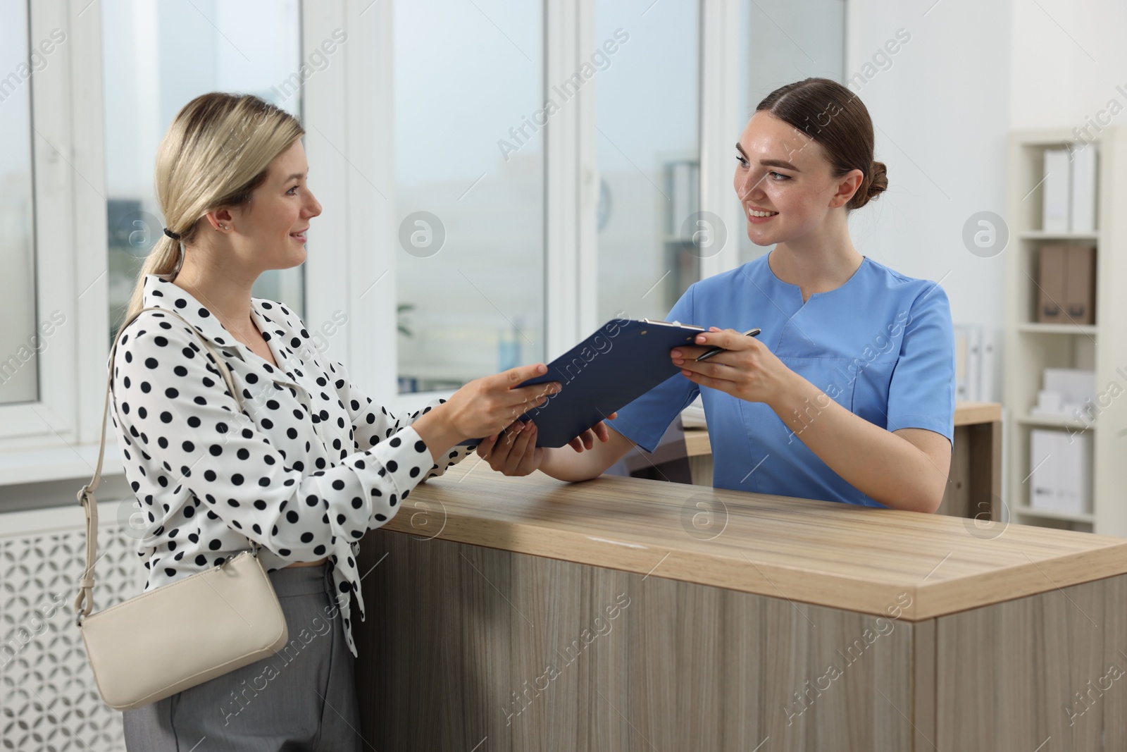 Photo of Professional receptionist working with patient at wooden desk in hospital