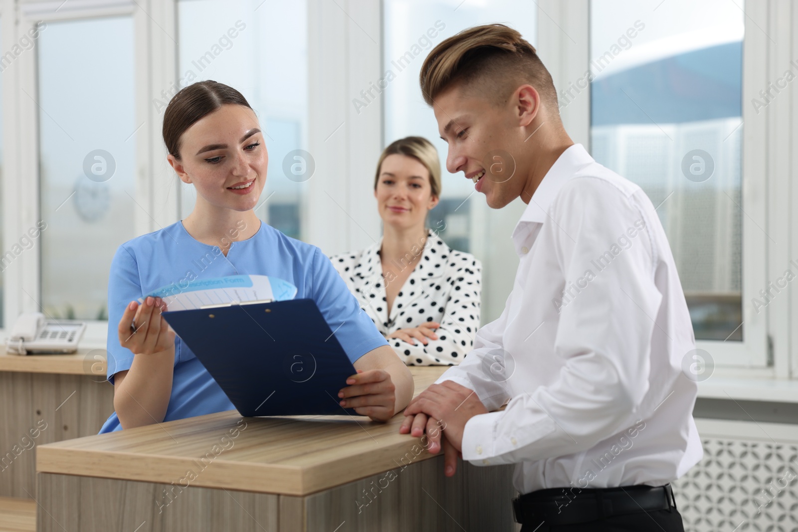 Photo of Professional receptionist working with patients at wooden desk in hospital