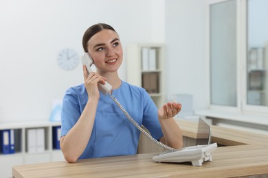 Photo of Professional receptionist talking on phone at wooden desk in hospital