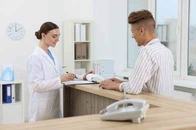 Photo of Professional receptionist working with patient at wooden desk in hospital