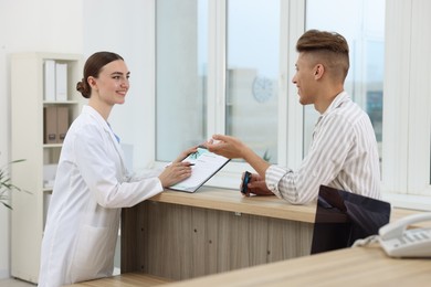 Photo of Professional receptionist working with patient at wooden desk in hospital