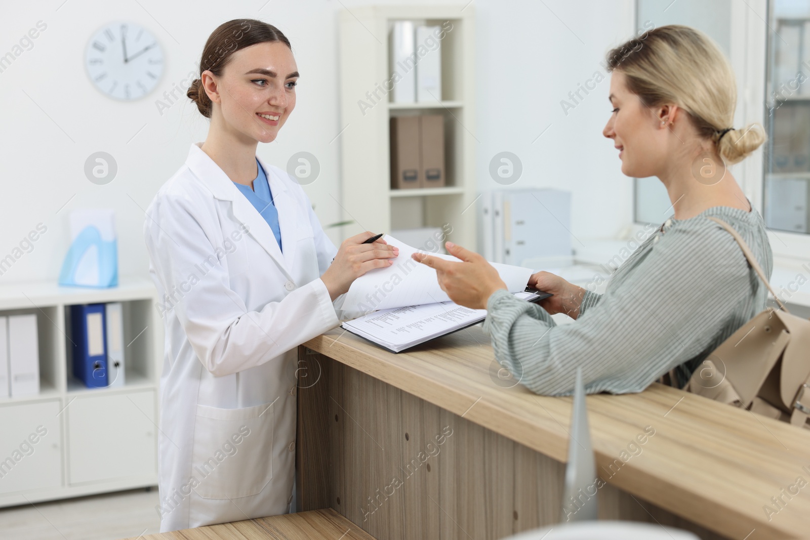 Photo of Professional receptionist working with patient at wooden desk in hospital