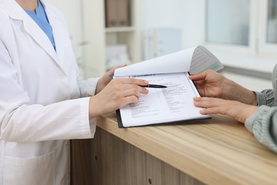 Photo of Professional receptionist working with patient at wooden desk in hospital, closeup