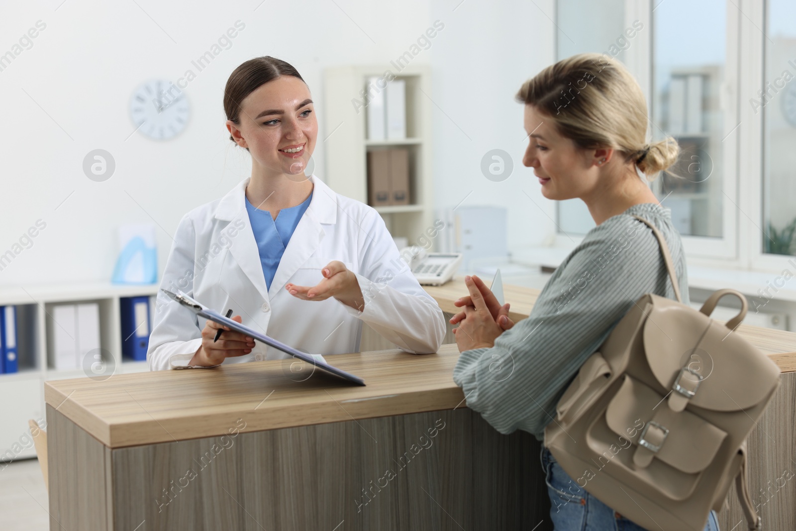 Photo of Professional receptionist working with patient at wooden desk in hospital