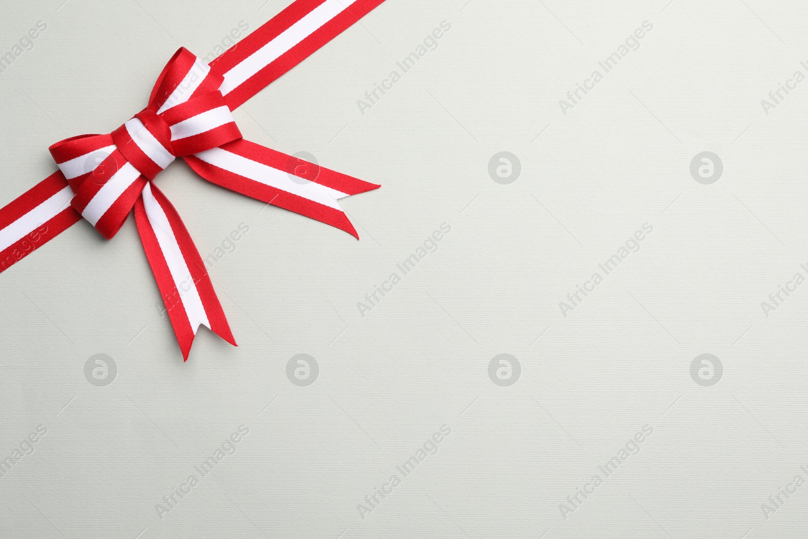 Photo of Ribbon with bow in colors of Austrian flag on light background, top view. Space for text