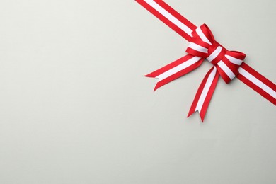 Photo of Ribbon with bow in colors of Austrian flag on light background, top view. Space for text