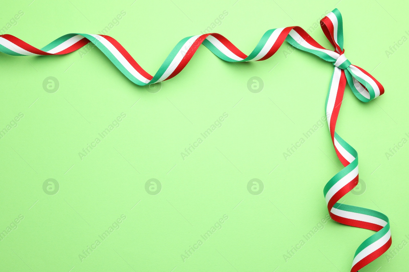 Photo of Ribbon with bow in colors of Hungarian flag on green background, top view. Space for text