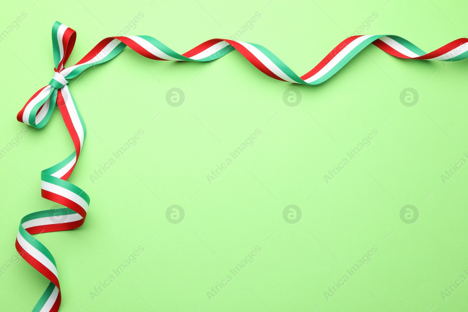 Photo of Ribbon with bow in colors of Hungarian flag on green background, top view. Space for text