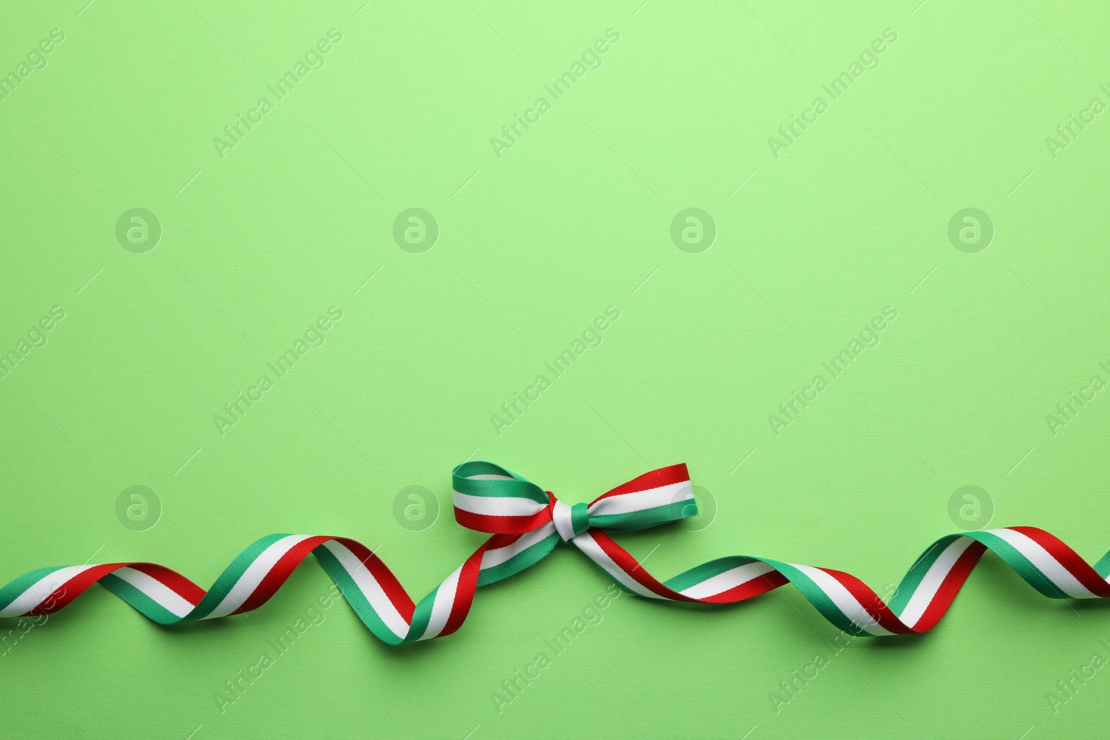 Photo of Ribbon with bow in colors of Hungarian flag on green background, top view. Space for text