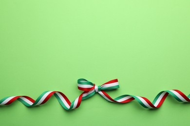 Ribbon with bow in colors of Hungarian flag on green background, top view. Space for text